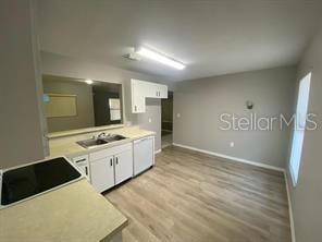 kitchen featuring a sink, light countertops, light wood-type flooring, white cabinetry, and baseboards