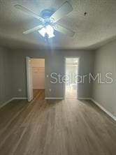 unfurnished bedroom featuring baseboards, wood finished floors, ceiling fan, and a walk in closet