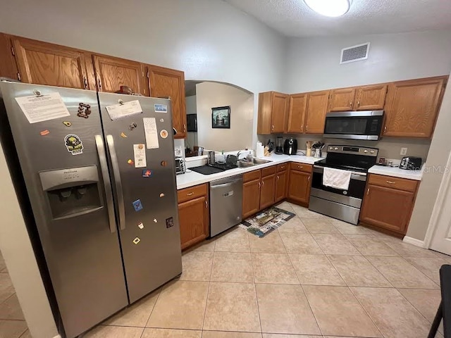 kitchen with arched walkways, light tile patterned floors, stainless steel appliances, light countertops, and vaulted ceiling
