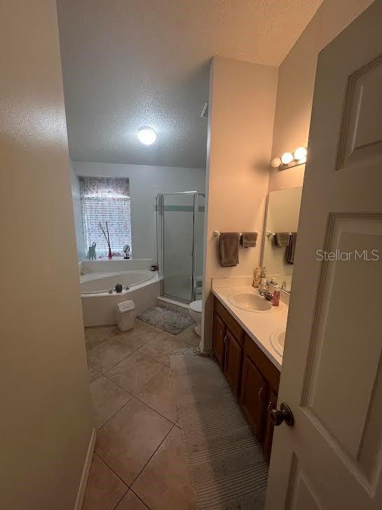 bathroom featuring tile patterned flooring, a textured ceiling, double vanity, a stall shower, and a garden tub