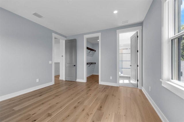 unfurnished bedroom featuring visible vents, a spacious closet, light wood-style flooring, and baseboards