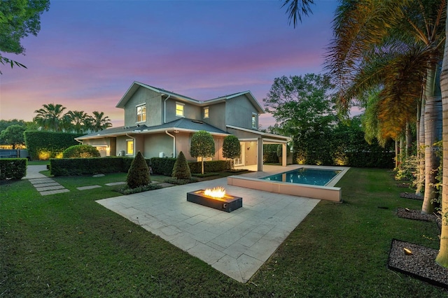 back of house at dusk featuring a patio, a lawn, stucco siding, and an outdoor fire pit
