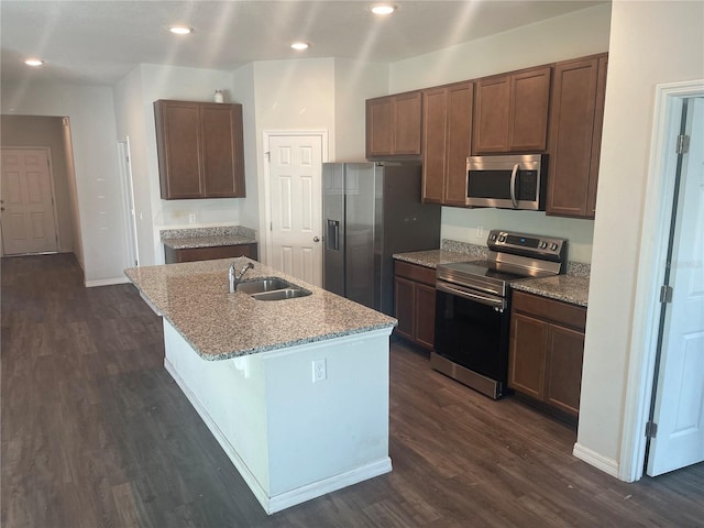 kitchen featuring an island with sink, light stone counters, stainless steel appliances, dark wood-style flooring, and a sink
