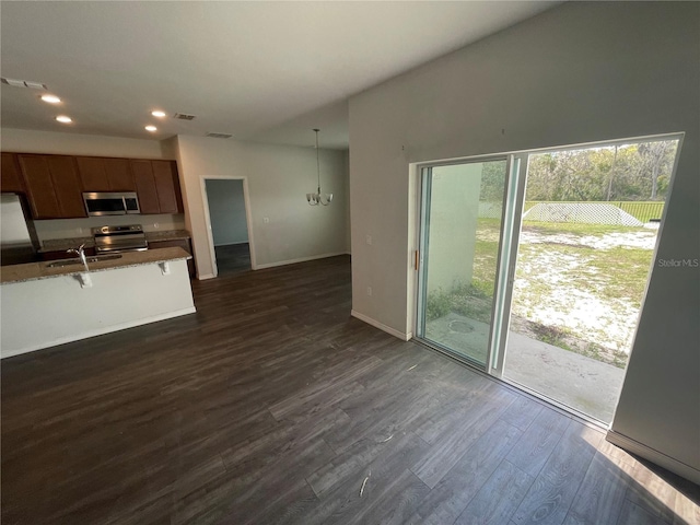 unfurnished living room with a sink, baseboards, recessed lighting, dark wood-type flooring, and a notable chandelier