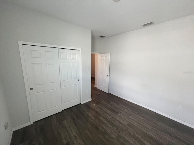 unfurnished bedroom featuring dark wood-style floors, a closet, visible vents, and baseboards