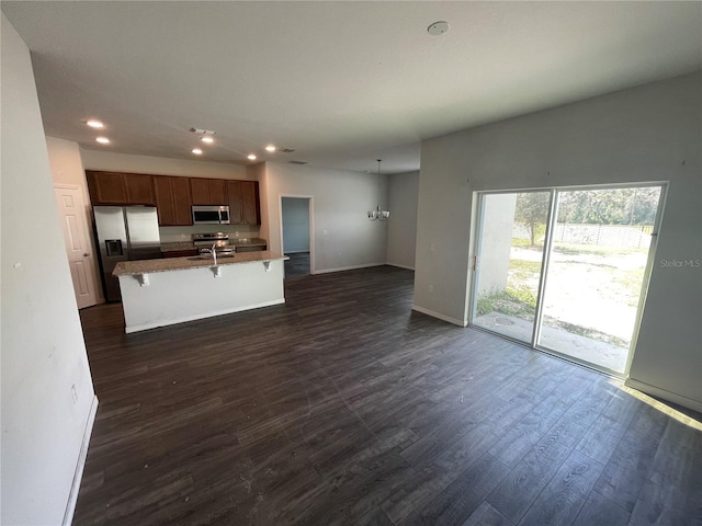 kitchen with appliances with stainless steel finishes, a breakfast bar, baseboards, recessed lighting, and dark wood-type flooring