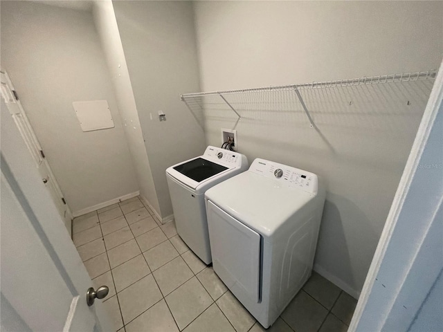 clothes washing area with light tile patterned floors, separate washer and dryer, laundry area, and baseboards