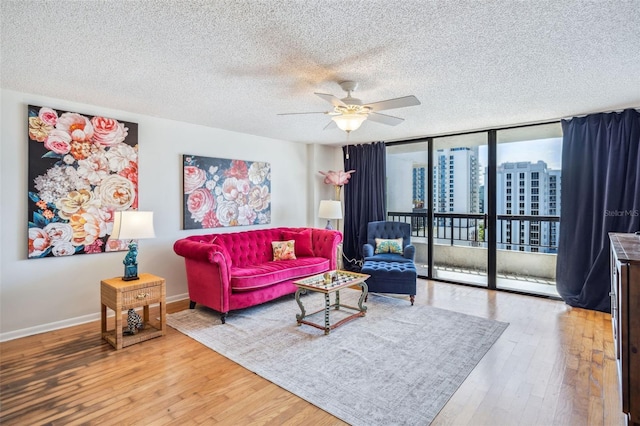 living room featuring wood-type flooring, a textured ceiling, a ceiling fan, baseboards, and floor to ceiling windows