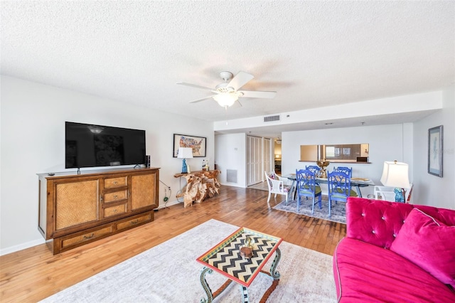 living room with a ceiling fan, a textured ceiling, visible vents, wood finished floors, and baseboards
