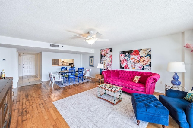 living room with a ceiling fan, a textured ceiling, visible vents, wood finished floors, and baseboards