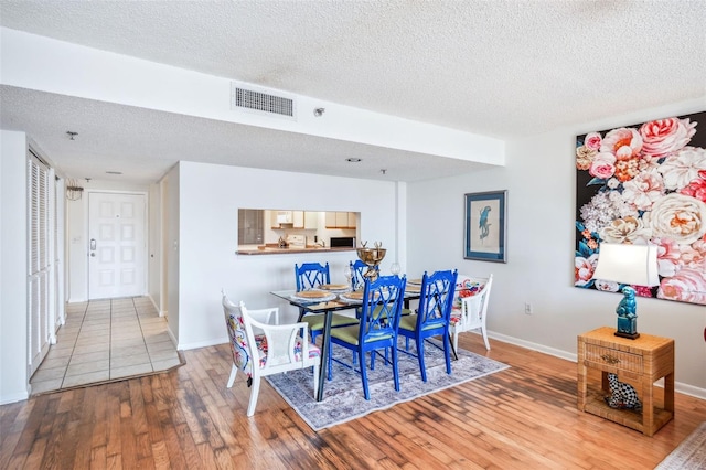 dining area with visible vents, a textured ceiling, wood-type flooring, and baseboards