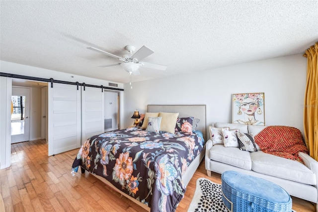bedroom with a ceiling fan, a textured ceiling, visible vents, a barn door, and light wood-style flooring