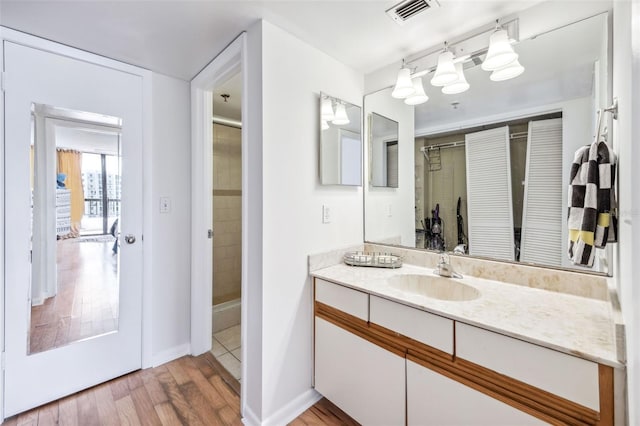 full bath featuring vanity, tiled shower, wood finished floors, and visible vents
