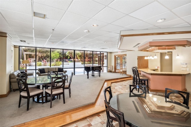 carpeted dining space with visible vents, baseboards, a drop ceiling, a community bar, and expansive windows