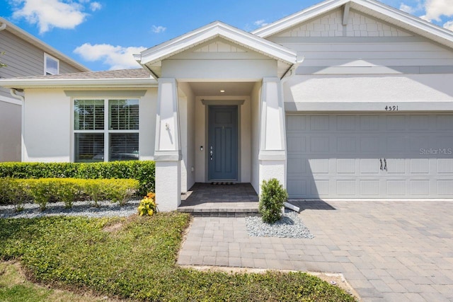 entrance to property with stucco siding, driveway, and a garage