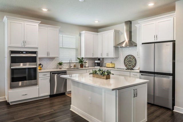 kitchen with a sink, light countertops, dark wood-style floors, stainless steel appliances, and wall chimney exhaust hood