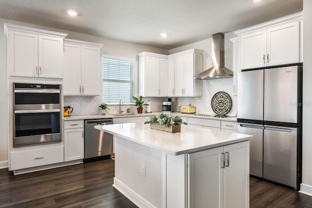 kitchen with backsplash, appliances with stainless steel finishes, a sink, wall chimney exhaust hood, and dark wood-type flooring