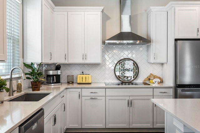 kitchen featuring wall chimney range hood, white cabinets, tasteful backsplash, a sink, and stainless steel appliances