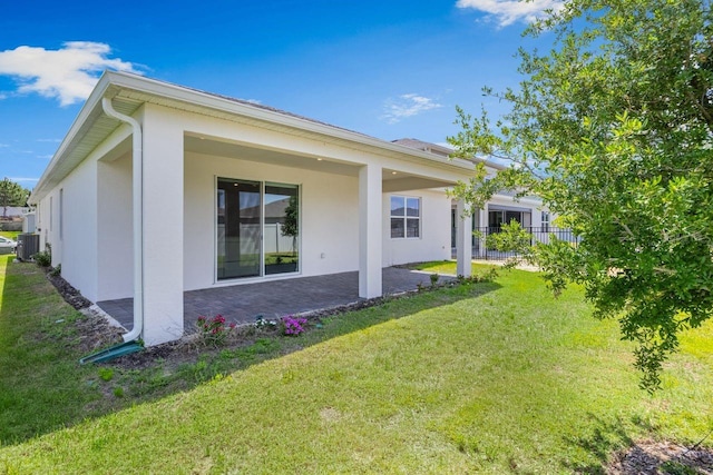 rear view of property with fence, stucco siding, cooling unit, a patio area, and a yard