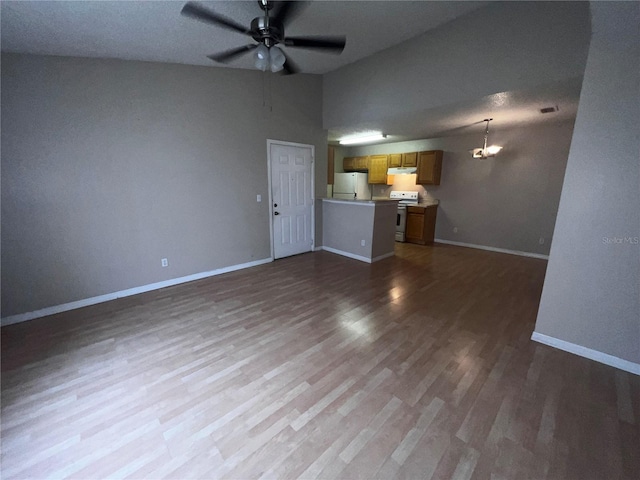 unfurnished living room with visible vents, wood finished floors, baseboards, ceiling fan with notable chandelier, and lofted ceiling