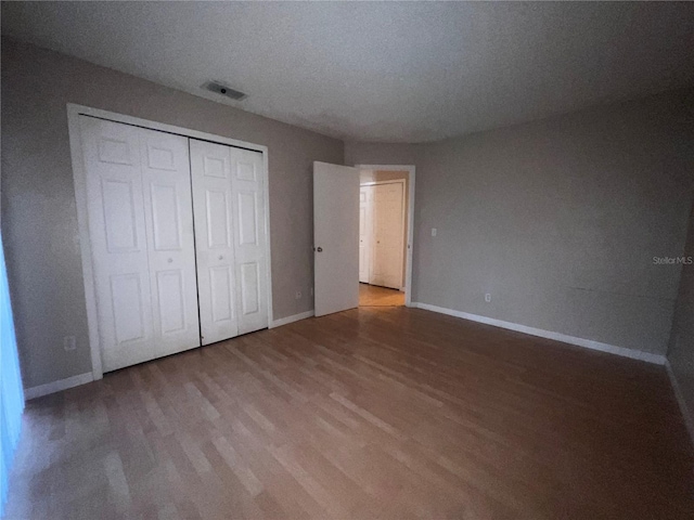 unfurnished bedroom featuring visible vents, baseboards, wood finished floors, and a closet