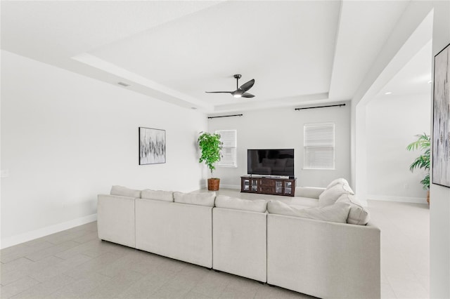 living area featuring a ceiling fan, baseboards, and a raised ceiling