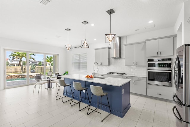 kitchen featuring wall chimney range hood, decorative backsplash, a sink, a breakfast bar, and stainless steel appliances