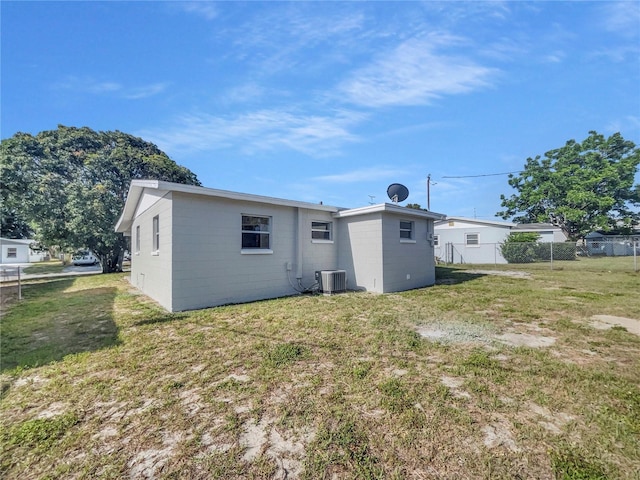 rear view of property with fence, concrete block siding, cooling unit, and a lawn