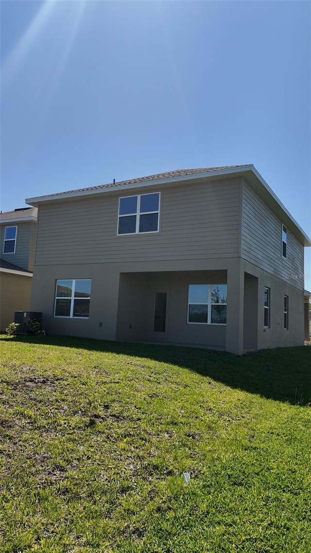 rear view of house with a lawn, central AC unit, and stucco siding