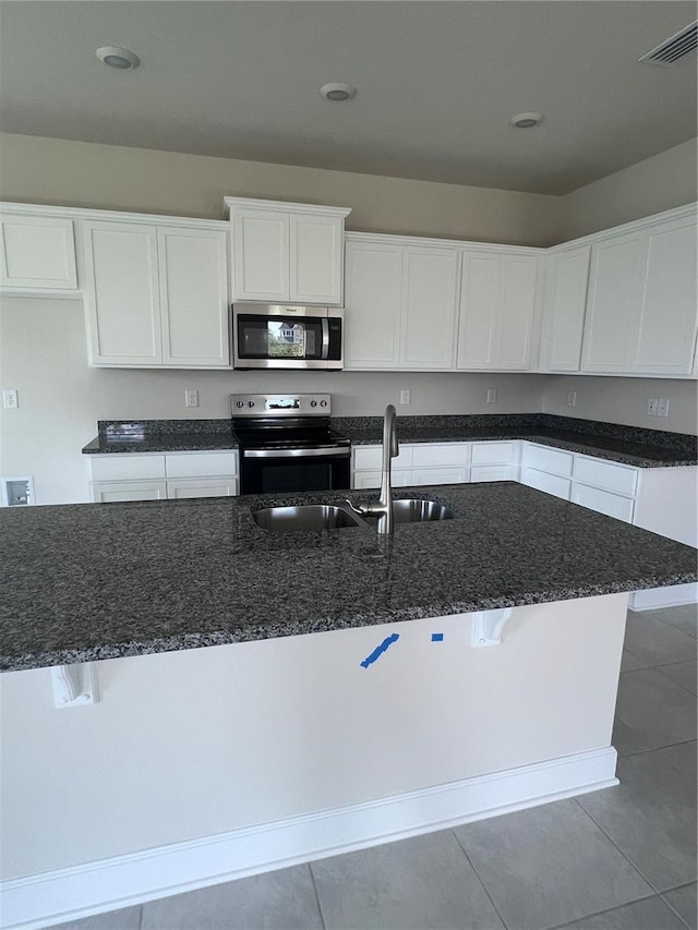 kitchen featuring visible vents, appliances with stainless steel finishes, tile patterned flooring, a sink, and dark stone counters
