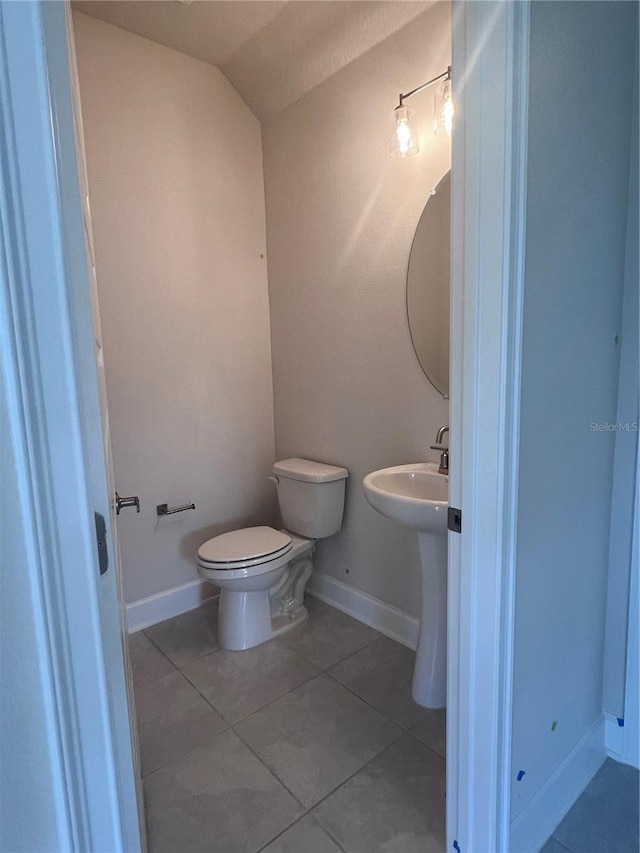 half bath featuring tile patterned flooring, baseboards, lofted ceiling, and toilet