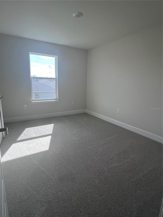 spare room featuring baseboards and dark carpet