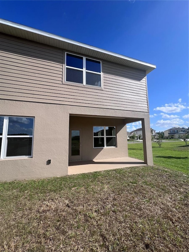back of property featuring a lawn, stucco siding, and a patio area