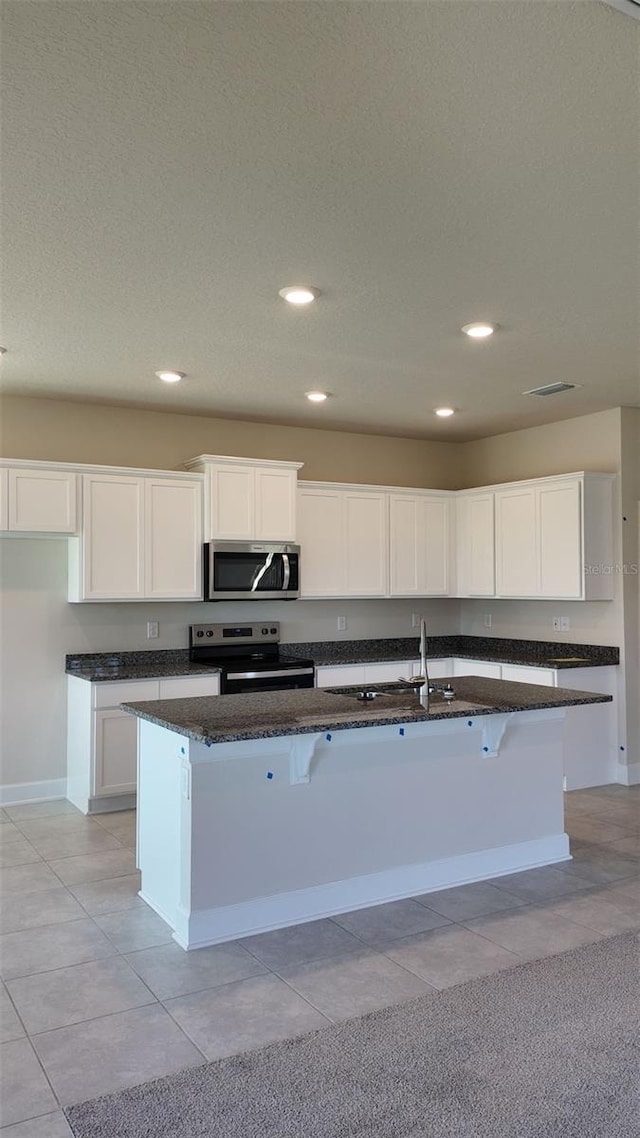 kitchen with dark stone counters, stainless steel appliances, white cabinets, and a breakfast bar