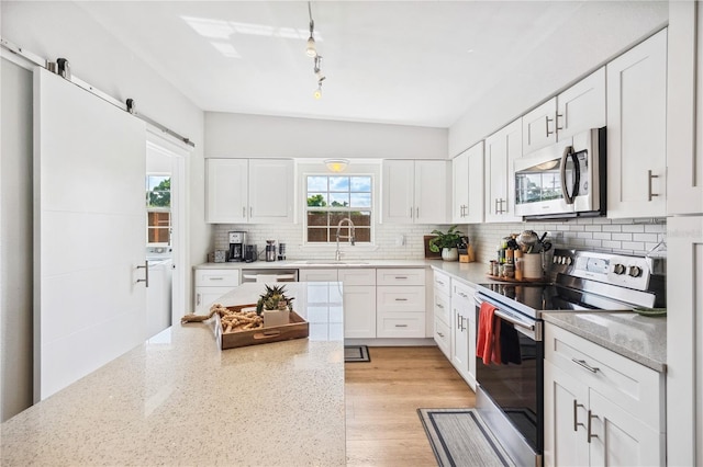 kitchen with backsplash, independent washer and dryer, a barn door, a sink, and stainless steel appliances
