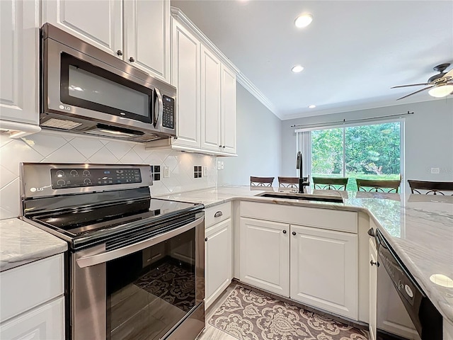 kitchen with decorative backsplash, white cabinets, a sink, appliances with stainless steel finishes, and ornamental molding