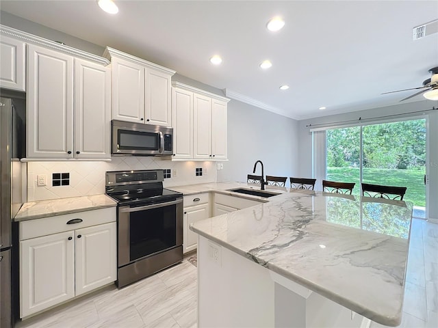 kitchen with a sink, a peninsula, backsplash, ornamental molding, and appliances with stainless steel finishes