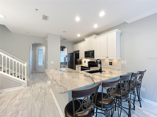 kitchen featuring light stone countertops, arched walkways, stainless steel appliances, a sink, and baseboards
