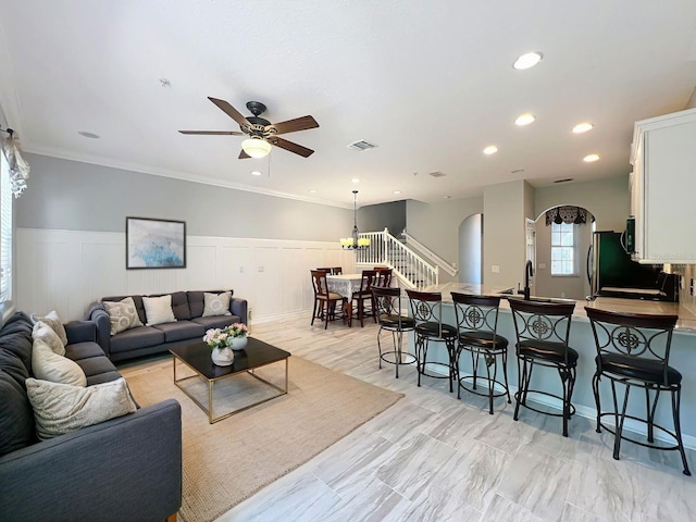 living area featuring crown molding, a wainscoted wall, visible vents, and ceiling fan