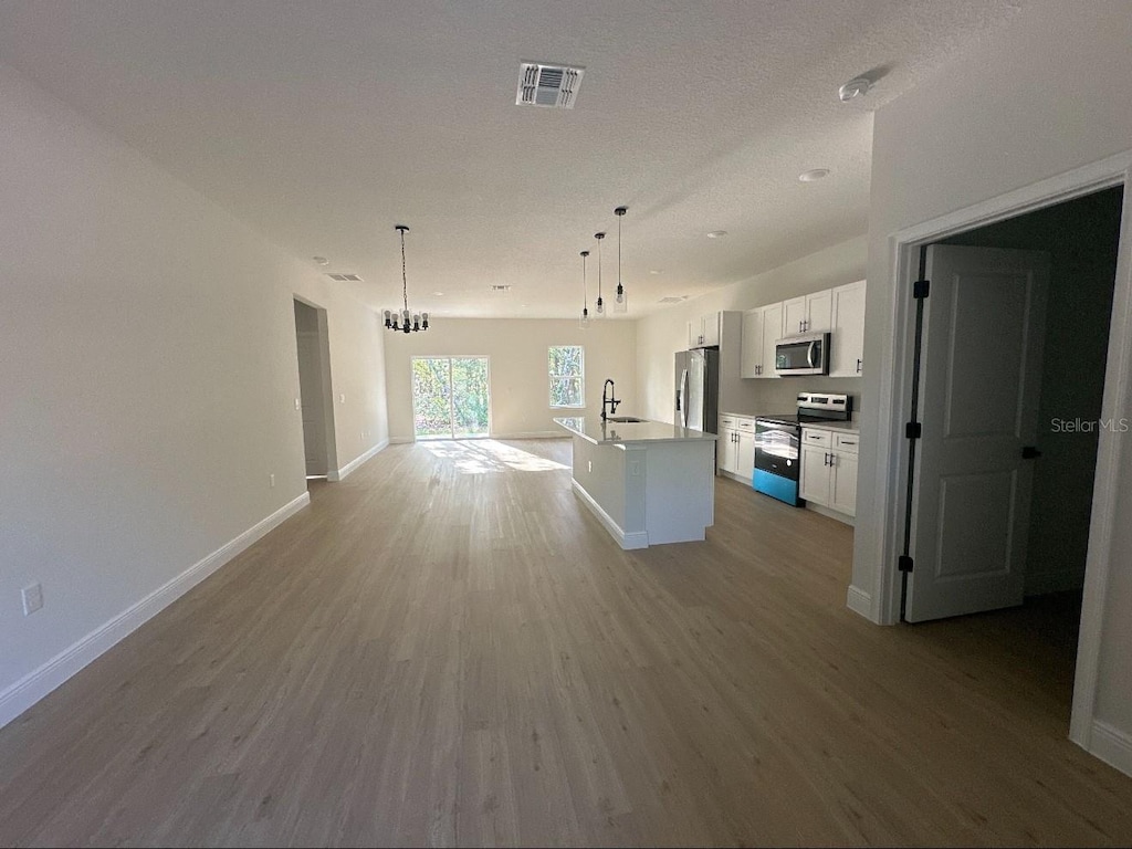 14957 SW 63rd Court Rd, Ocala, FL 34473 - kitchen with appliances with stainless steel finishes, a kitchen island with sink, white cabinets, light wood finished floors, and open floor plan