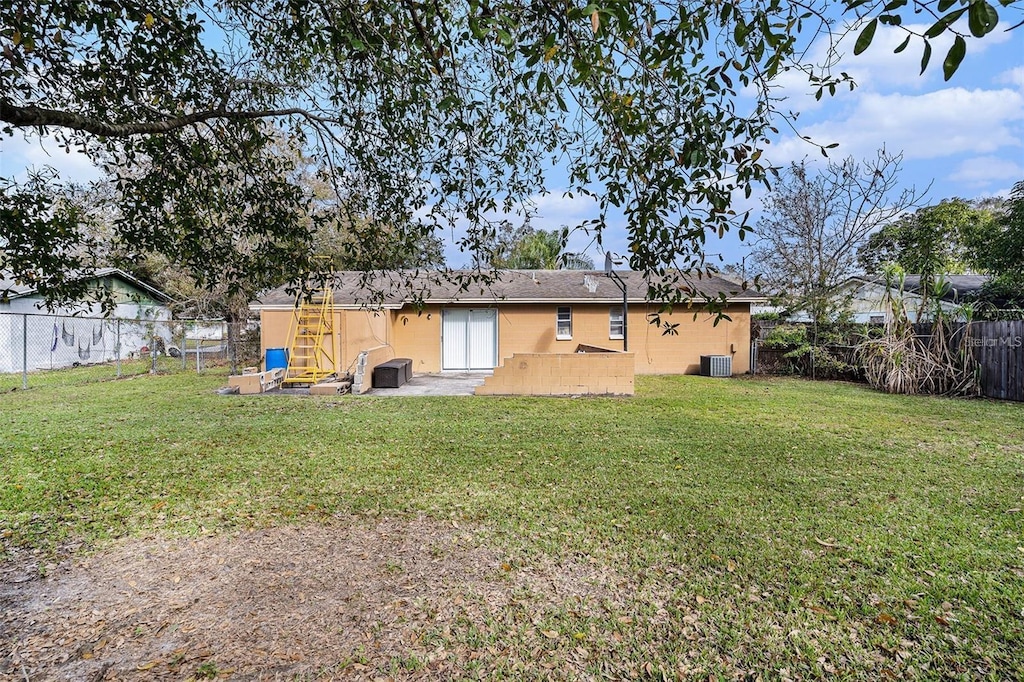 rear view of house with a lawn, a shingled roof, a fenced backyard, and central air condition unit