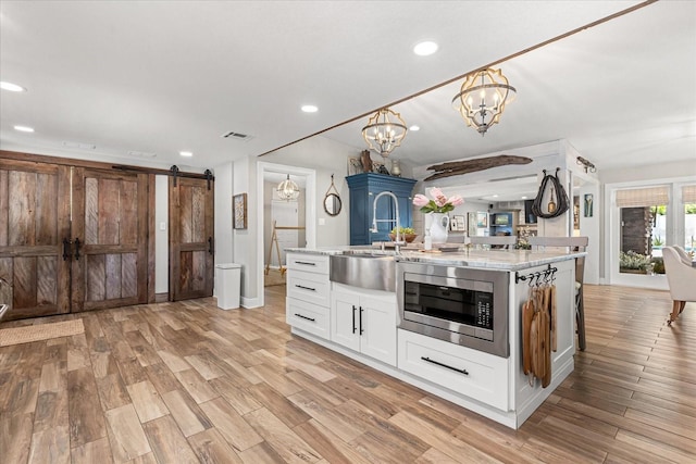 2105 Fosgate Dr, Winter Park, FL 32789 - kitchen featuring stainless steel microwave, a sink, a barn door, light wood-style flooring, and white cabinets