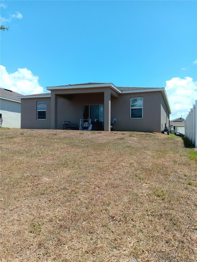 back of property with a lawn and stucco siding