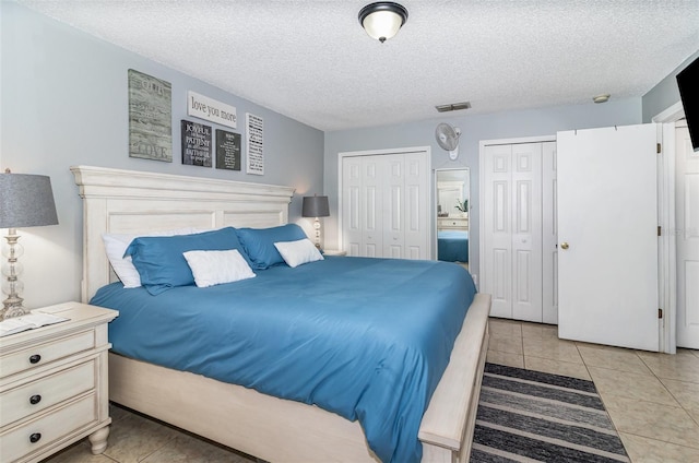 bedroom with light tile patterned floors, multiple closets, a textured ceiling, and visible vents