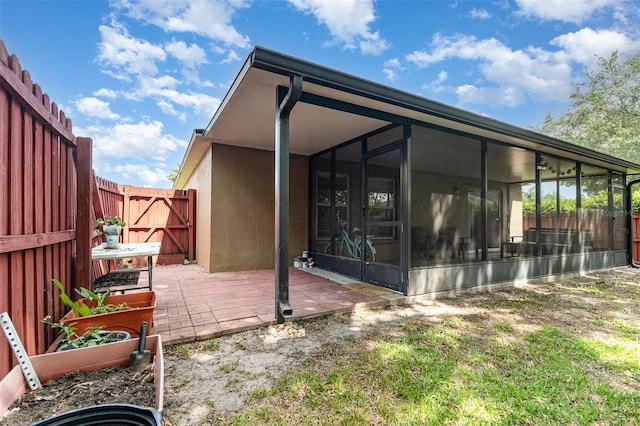 rear view of house featuring a vegetable garden, a fenced backyard, a sunroom, and stucco siding