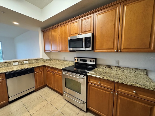 6336 Buford St Unit 307, Orlando, FL 32835 - kitchen featuring light stone counters, brown cabinetry, stainless steel appliances, and light tile patterned flooring