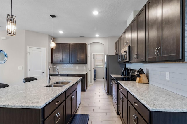 kitchen with dark brown cabinetry, a sink, a textured ceiling, stainless steel appliances, and decorative backsplash