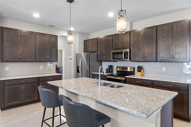 kitchen with visible vents, dark brown cabinetry, a breakfast bar, a sink, and appliances with stainless steel finishes
