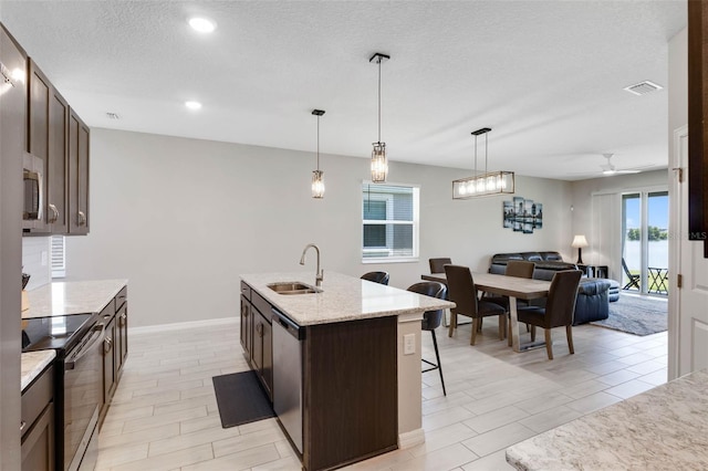 kitchen featuring dark brown cabinetry, appliances with stainless steel finishes, a sink, and a kitchen bar