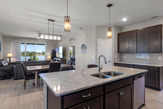 kitchen featuring dark brown cabinetry, a sink, dishwasher, arched walkways, and open floor plan